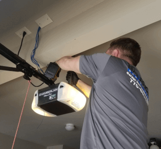 Technician servicing garage door mechanism on ceiling of garage.