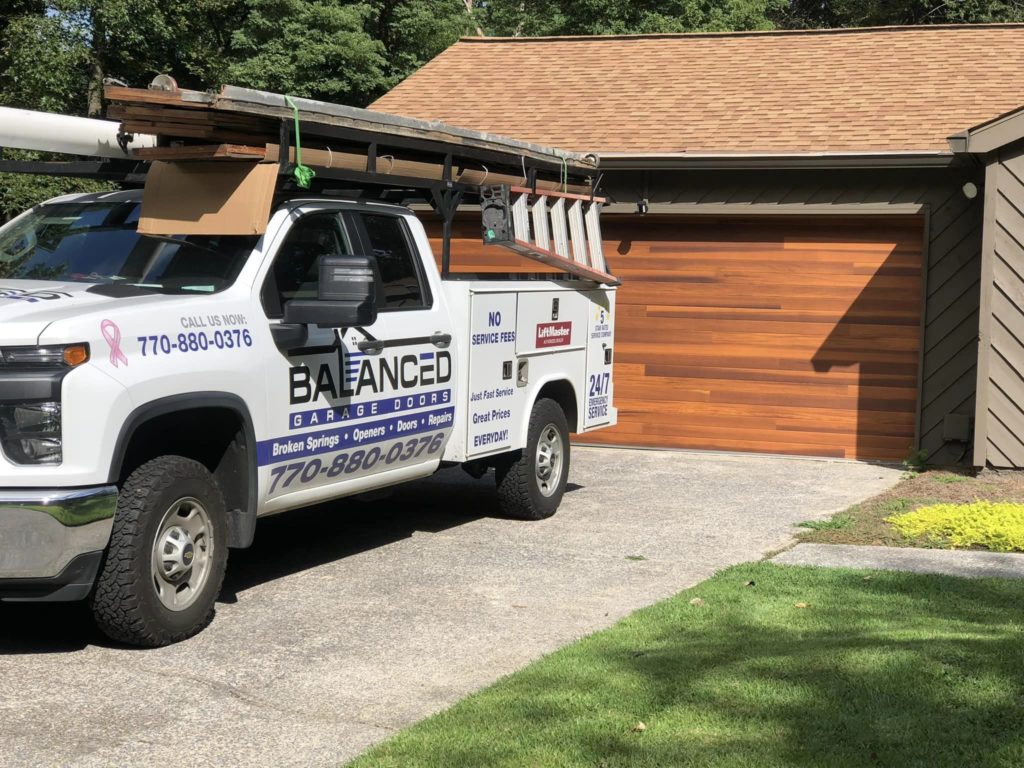 Balanced Garage Door truck parked in the driveway of a home with a wooden garage door