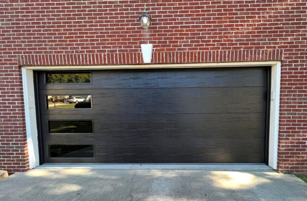 newly installed black garage door on a brick house, with horizontal windows down left side.