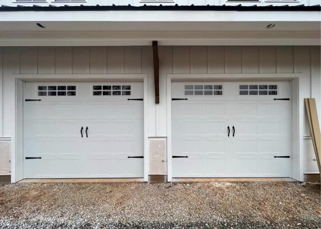 Newly installed white paneled double car garage doors with small windows in the top.