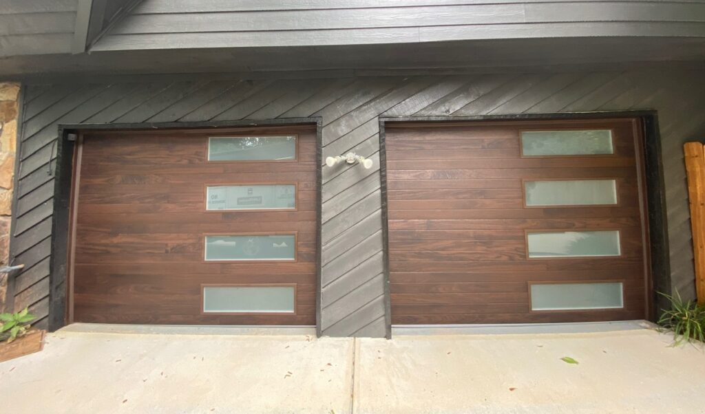 Two wooden, modern style garage doors with a row of rectangular windows down the right side of each, with fogged glass.