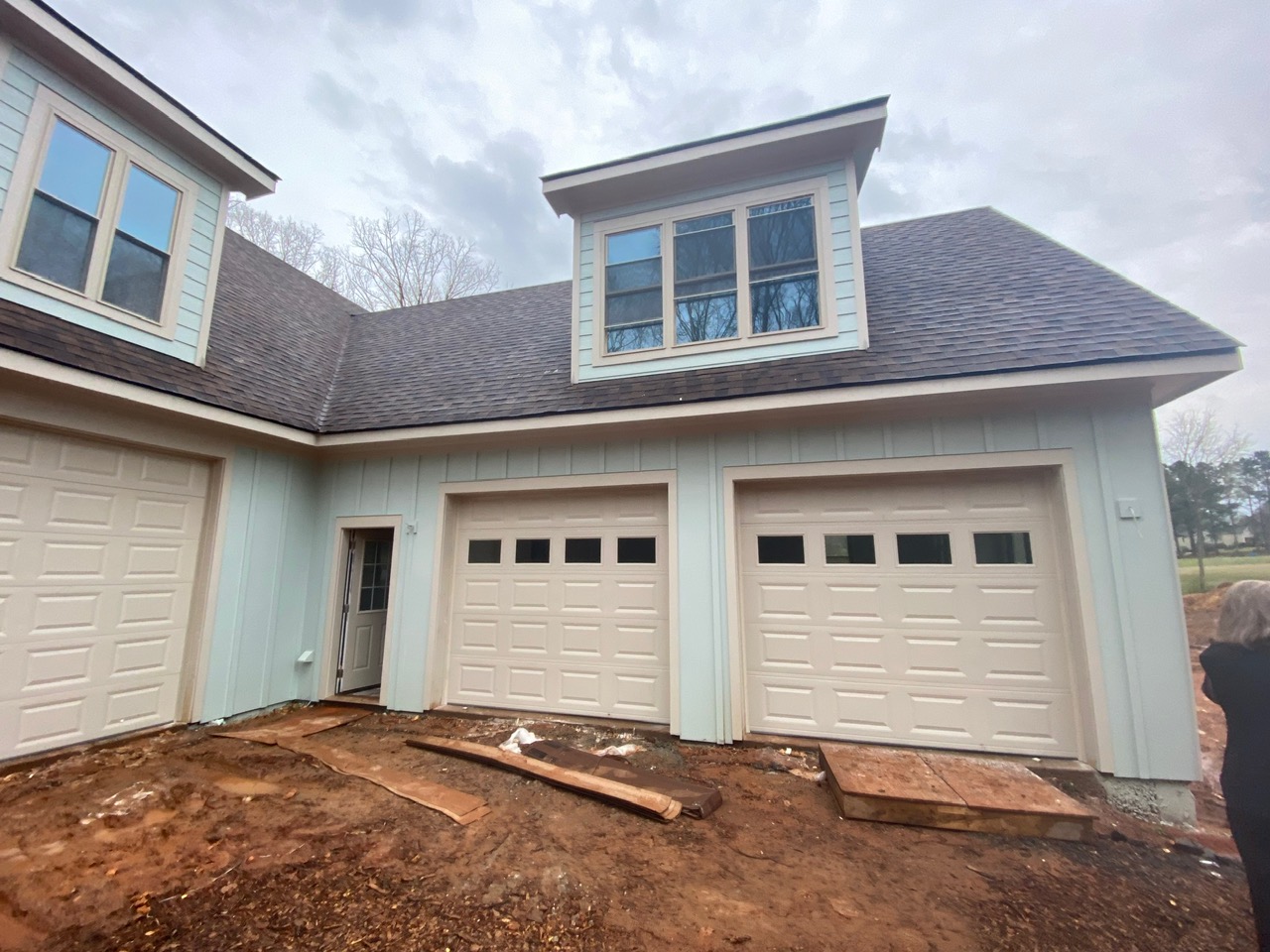 Two traditional off-white raised-panel garage doors on seafoam green house with unfinished driveway.